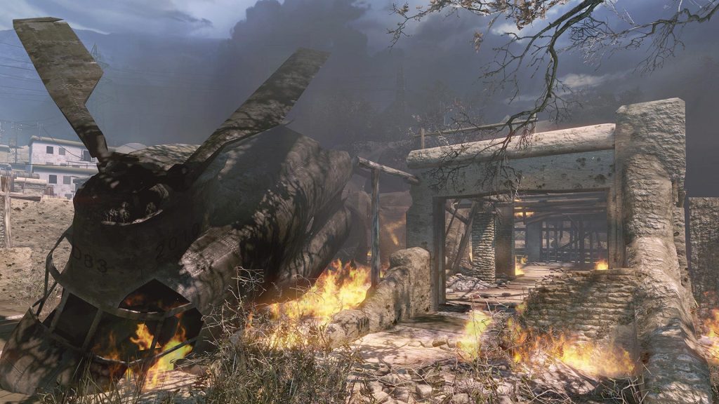 Burning crashed helicopter wreckage beside a ruined stone building under a stormy sky, in Warface